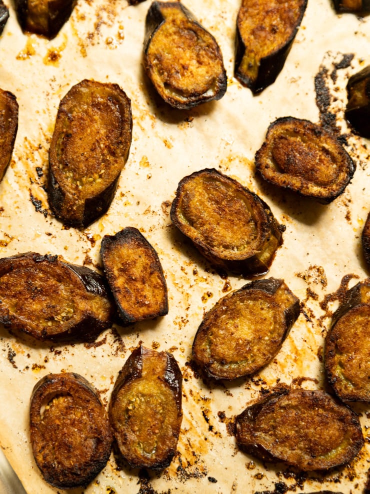 Close-up of roasted eggplant halves on a baking sheet, cut sides deeply browned and caramelized with charred edges.