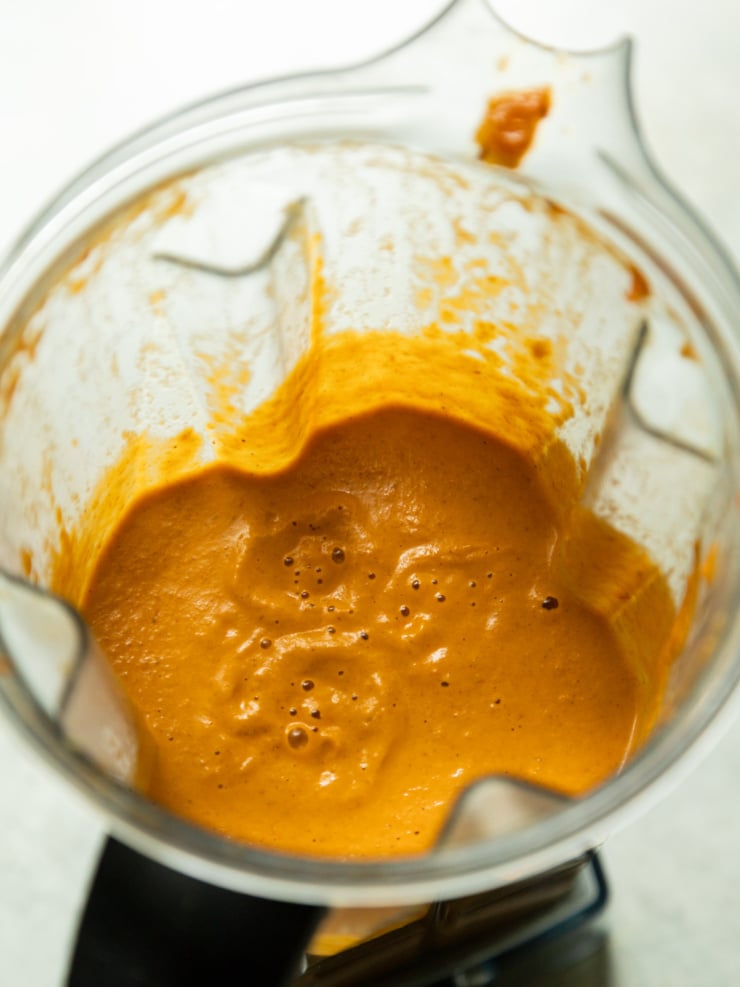 Overhead view of a blender jug filled with smooth, bright orange curry sauce, freshly blended.