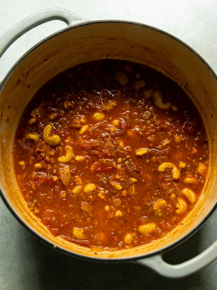 Overhead shot of a Dutch oven filled with simmering tomato curry sauce studded with cashews, before blending.