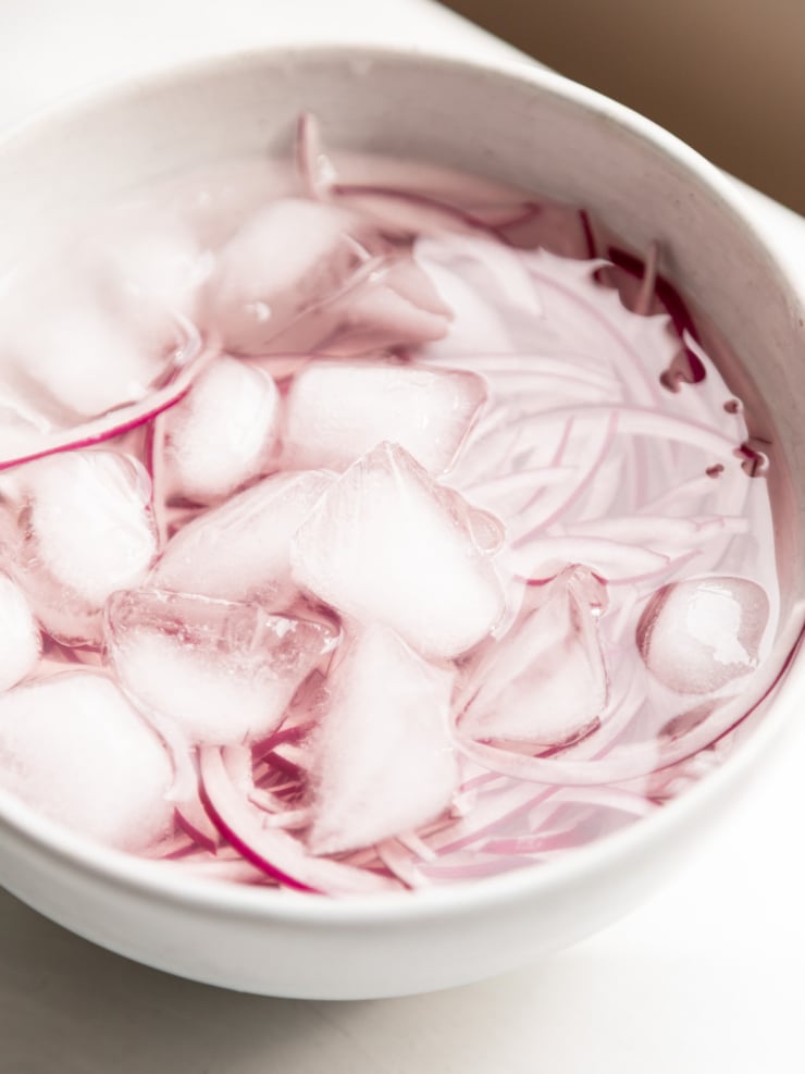 Thinly sliced red onion soaking in a bowl of ice water to mellow its sharpness.