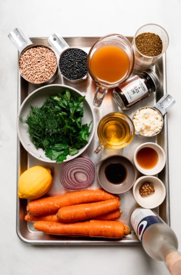 Ingredients for farro lentil salad on a tray: farro, black lentils, broth, za'atar, black lime, parsley, dill, olive oil, crumbled vegan feta, lemon, red onion, carrots and dressing ingredients.