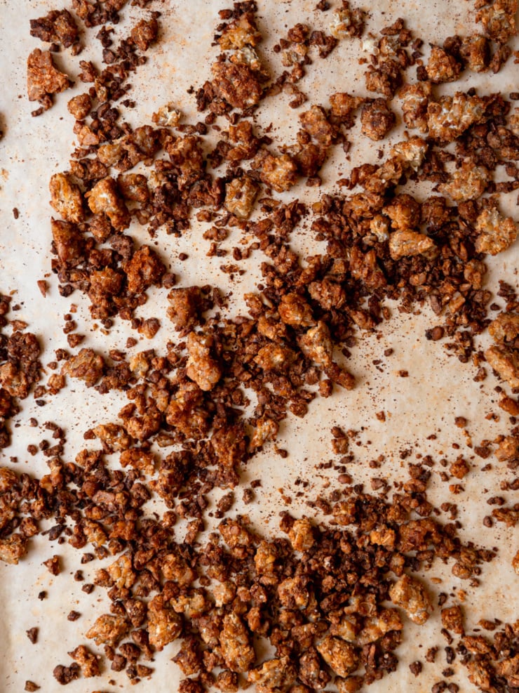 Crispy, deeply browned smoky tempeh crumbles spread across a parchment-lined baking sheet after roasting.