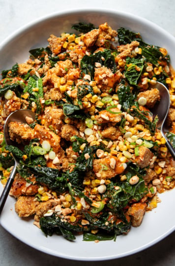 Overhead shot of spicy peanut kale salad with charred corn and crispy tofu, drizzled with peanut sauce and topped with chopped peanuts and scallions.