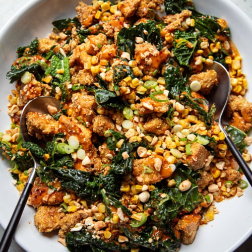 Overhead shot of spicy peanut kale salad with charred corn and crispy tofu, drizzled with peanut sauce and topped with chopped peanuts and scallions.