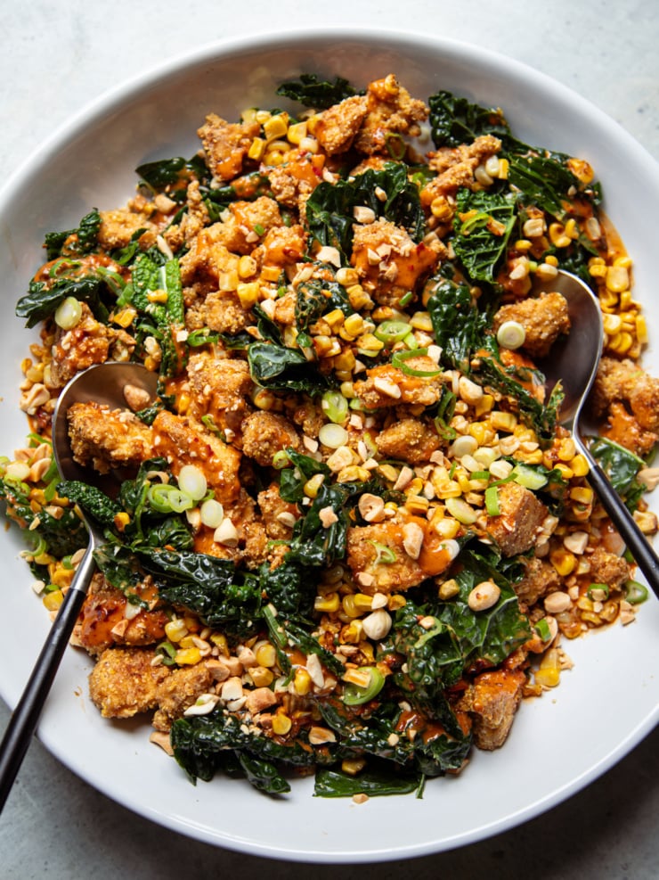 Overhead shot of spicy peanut kale salad with charred corn and crispy tofu, drizzled with peanut sauce and topped with chopped peanuts and scallions.