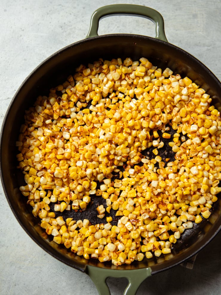 Charred corn kernels cooking in a cast iron skillet, developing golden-brown spots.