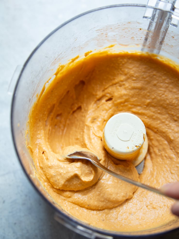 A spoon swoops through creamy orange butternut squash dip in a food processor.