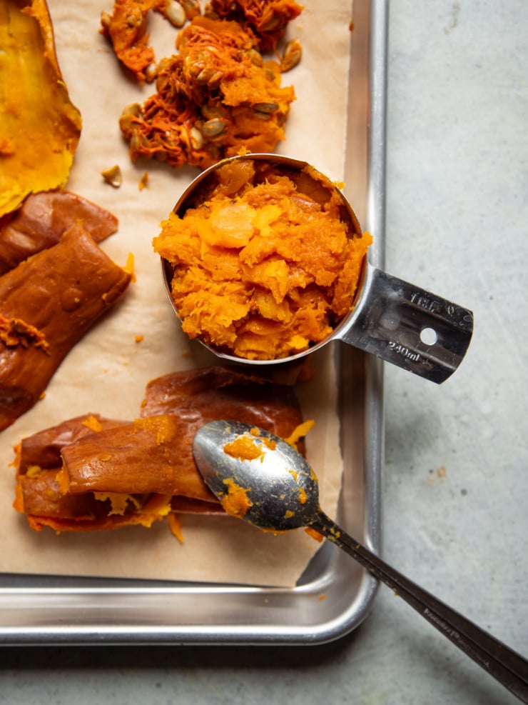 Roasted honeynut squash flesh packed into a 1-cup measure on a parchment-lined sheet pan, with the scooped-out skins and seeds beside it.