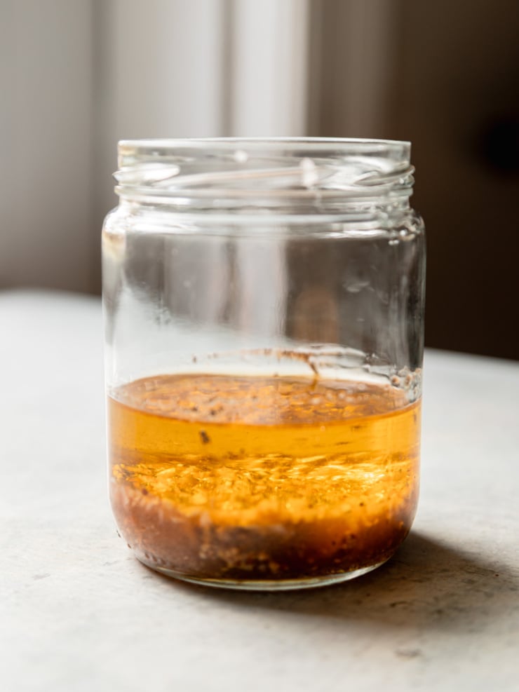 A glass jar of sherry maple vinaigrette, with minced shallot and mustard seeds settled at the bottom.