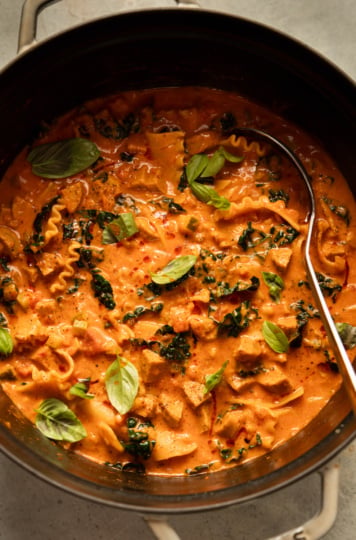 Overhead view of a pot of vegan lasagna soup with a ladle, garnished with fresh basil.