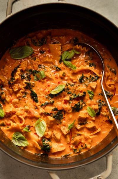 Overhead view of a pot of vegan lasagna soup with a ladle, garnished with fresh basil.