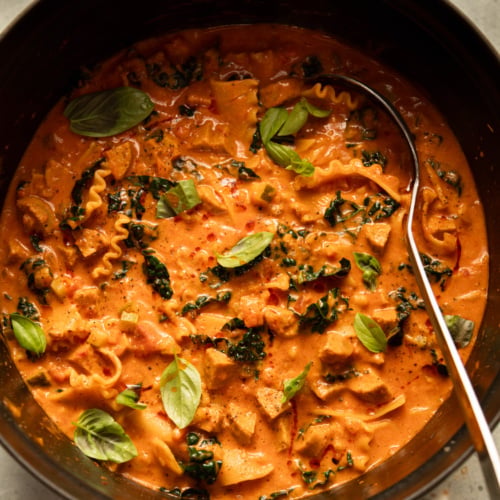 Overhead view of a pot of vegan lasagna soup with a ladle, garnished with fresh basil.