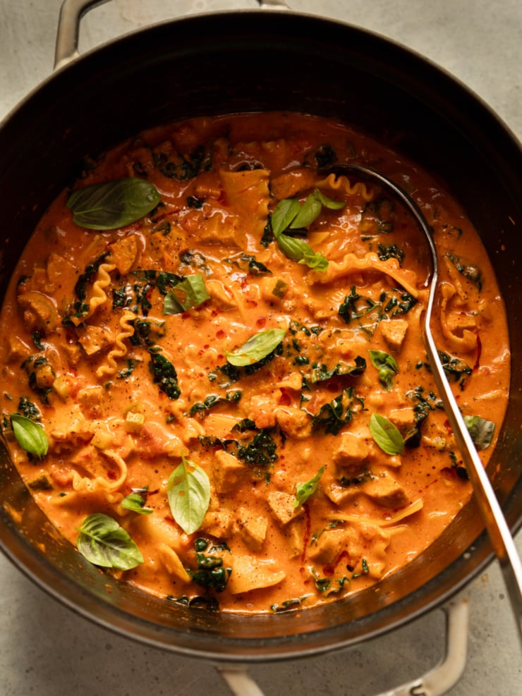 Overhead view of a pot of vegan lasagna soup with a ladle, garnished with fresh basil.