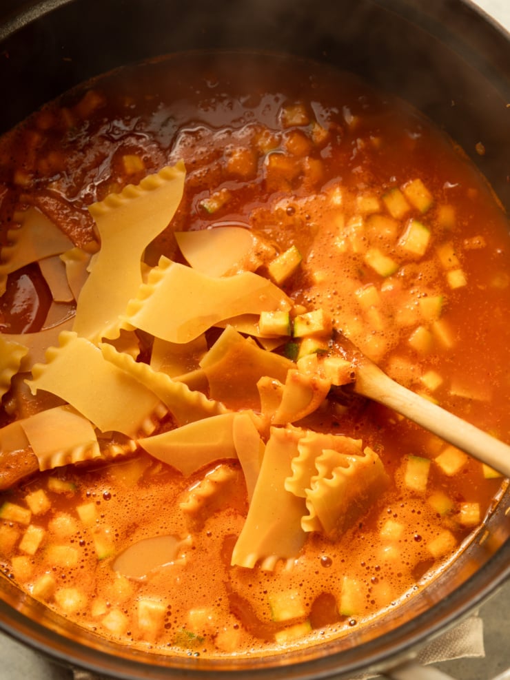 Broken lasagna noodles and diced zucchini simmering in tomato broth in a Dutch oven.