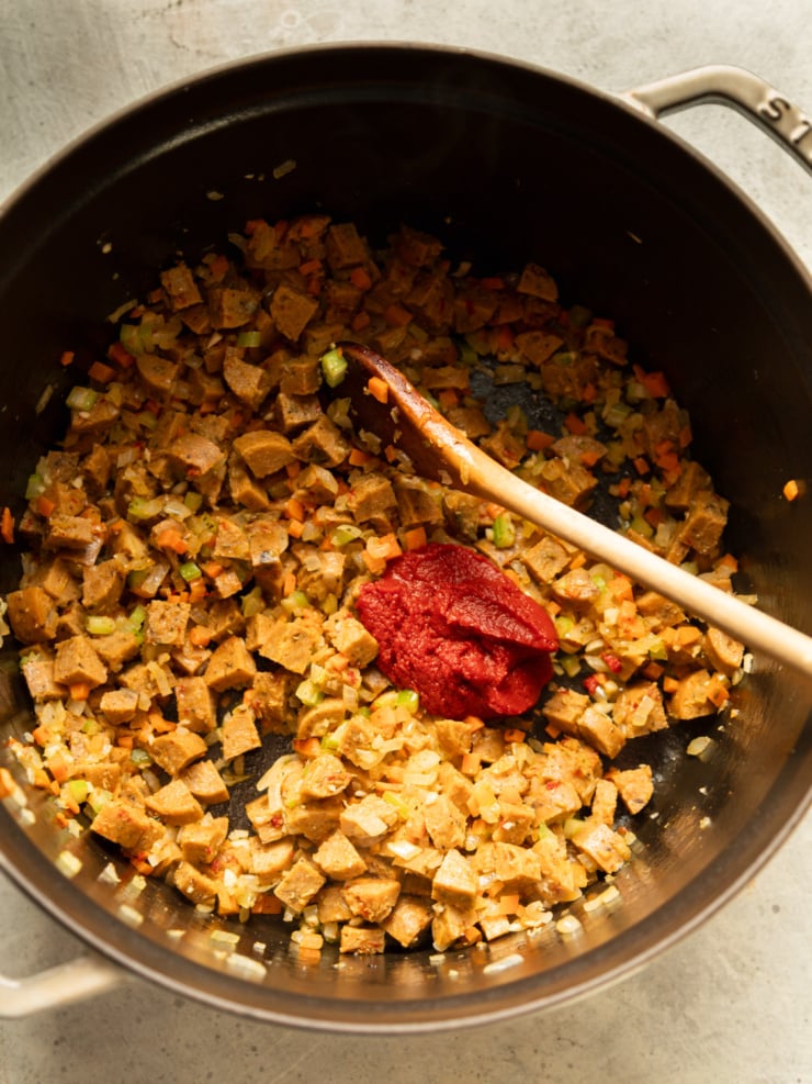 Sautéed veggie sausage, onion, carrot, and celery in a Dutch oven with a dollop of tomato paste.