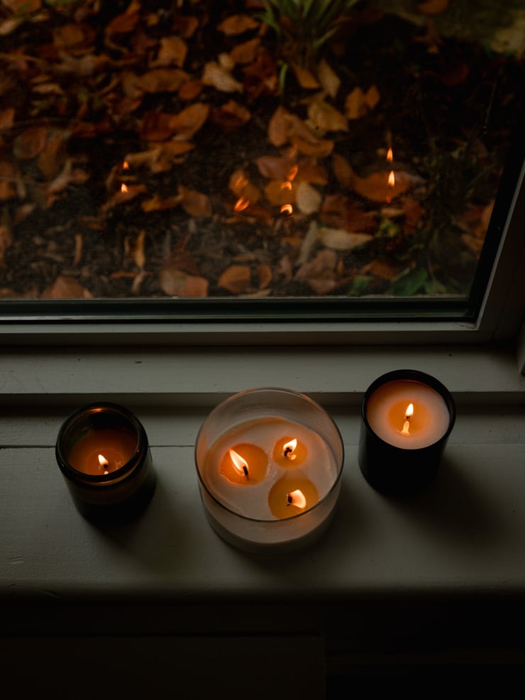 An overhead shot shows 3 candles in glass containers, all lit by a windowsill in very low light conditions.